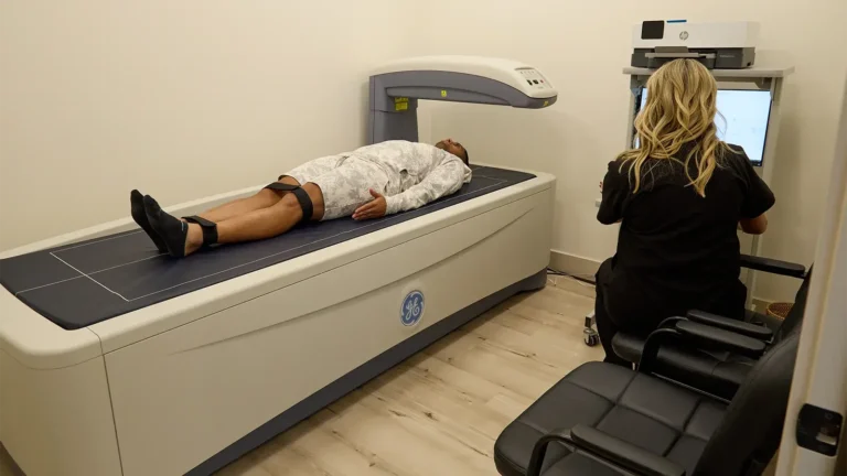Full body DEXA scan being performed on a man lying down while a female clinician looks on.
