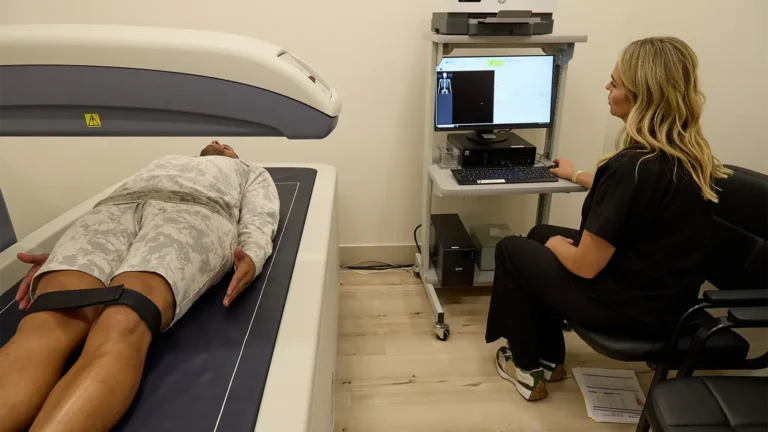 male client lying on a full body DEXA scan machine while female clinician sits nearby at a computer