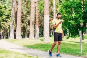 A man using his smartphone and listening to music in headphones while walking in the park